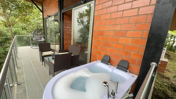 A spa area with a hot tub, wicker chairs, and a glass balustrade. - Samay Forest (Quito)