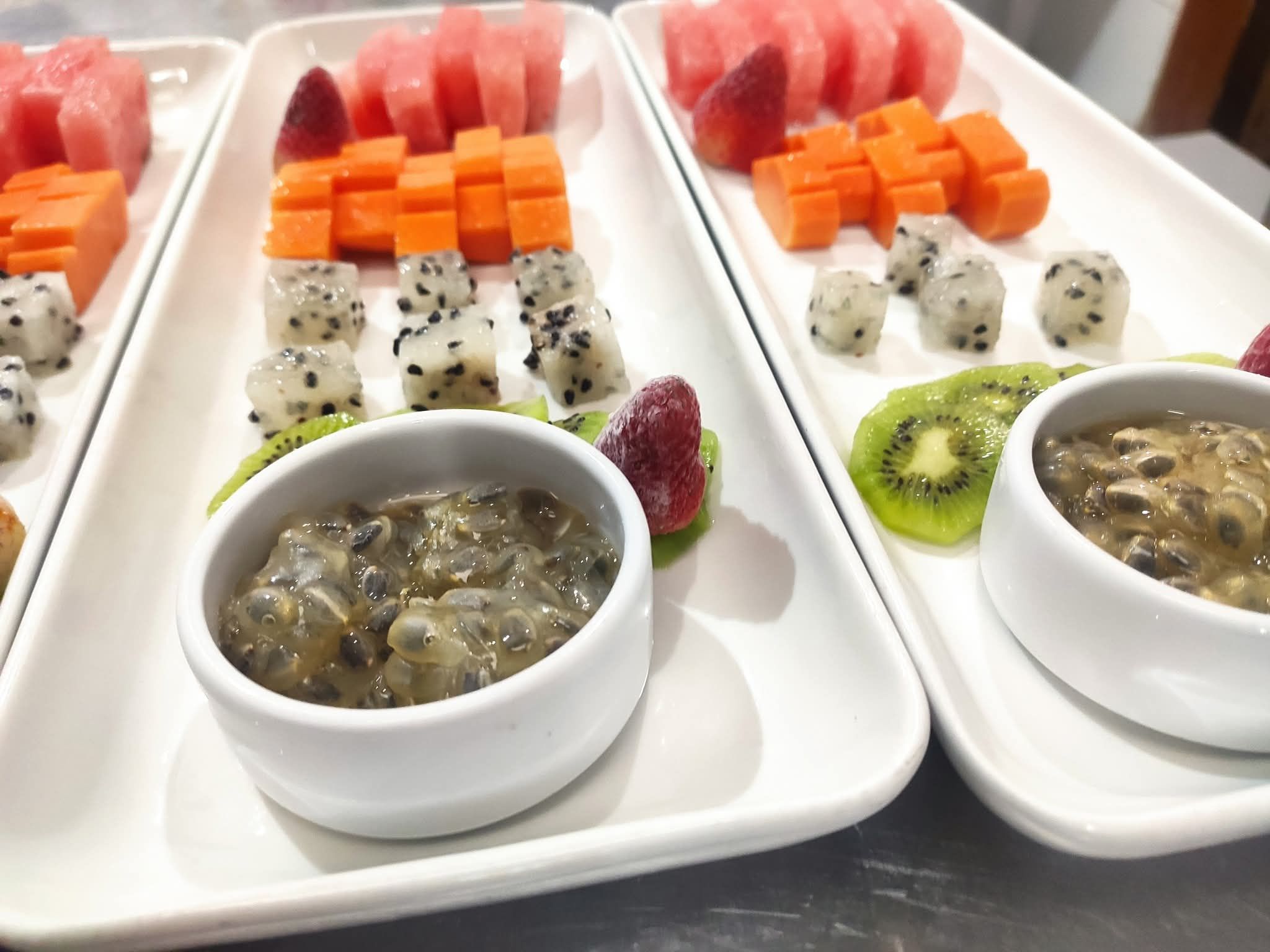 Un plateau blanc contenant divers aliments, notamment de la pastèque, de la mangue, du kiwi et deux bols d’un plat qui semble être à base de champignons.