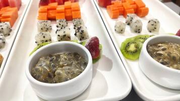 Un plateau blanc contenant divers aliments, notamment de la pastèque, de la mangue, du kiwi et deux bols d’un plat qui semble être à base de champignons.