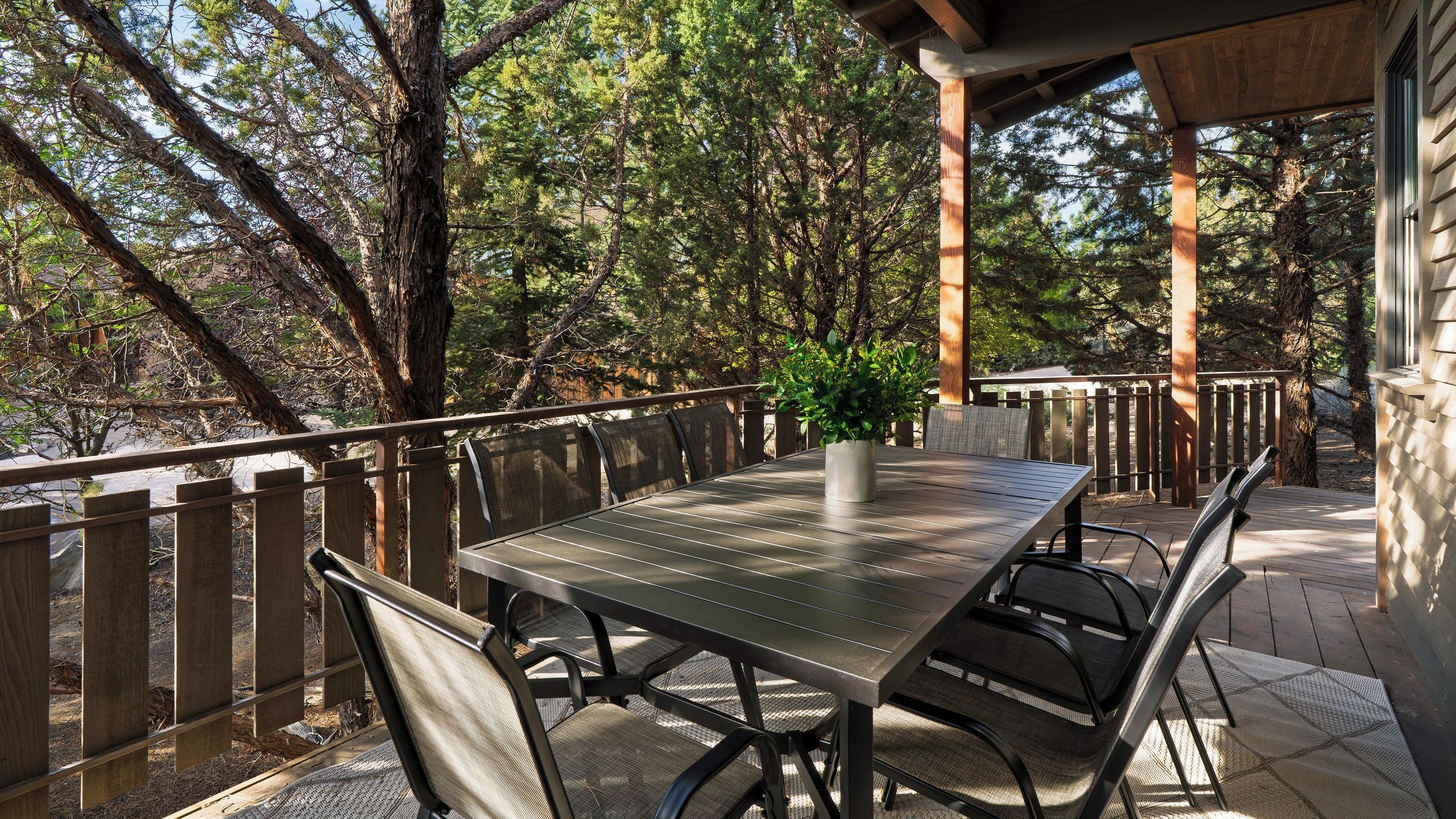 Un patio al aire libre con una mesa y sillas, rodeado por una valla de madera y árboles.