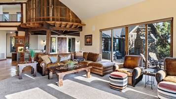 A spacious living room with a large wooden ceiling structure, leather furniture, and a view of the outside.