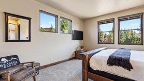 A bedroom with a bed, a bench, a small table, a TV, and windows with a view of trees. - The Water Tower House by Avantstay Tower Card Room + Casita + Game Room Panoramic Cascade Views (Powell Butte)