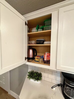 A kitchen cabinet with storage shelves containing kitchenware and food items. - The River House (Bismarck)