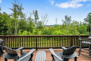 A wooden deck with outdoor furniture and a view of a forested landscape. - Loon Basecamp - Townhome Near Loon Mtn, Sleeps 12, Pools, Hot Tub, Game Room (Lincoln)