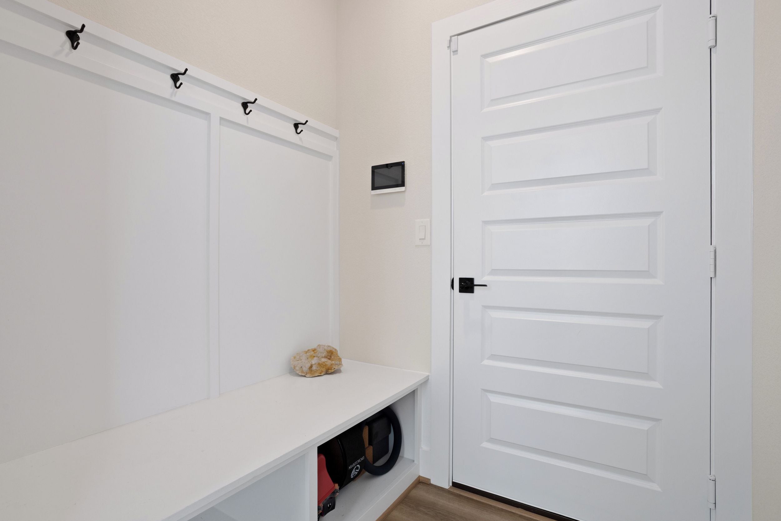 Eine weiße Tür mit schlichtem Design, eine kleine Ablage mit einem Stein und einem roten Gegenstand, sowie ein an der Wand befestigtes Gerät.