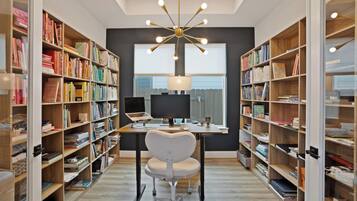 Uma biblioteca moderna com estantes de livros em ambos os lados, uma mesa com um laptop e uma luminária de teto singular.