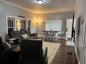 A living room with a sectional sofa, dining table with chairs, a lamp, and a window with blinds. - 1 mile to Bryant Denny Stadium (Tuscaloosa)