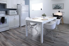 A modern kitchen with white cabinetry, a white dining table with four chairs, and a small potted plant on the table. - The Sweet Escape Okanagan (Kelowna)