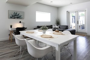 A modern dining area with a white table, four white chairs, and woven placemats. - The Sweet Escape Okanagan (Kelowna)