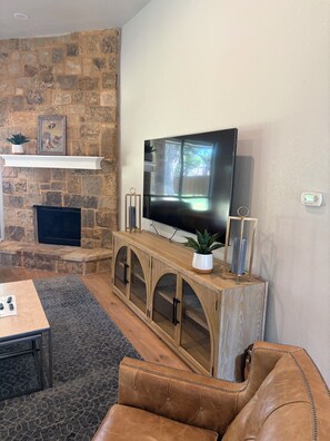 A living room with a stone fireplace, a flat-screen TV, a leather sofa, and a coffee table. - Lovely spacious Lake house on Eagle Mountain Lake in charming Fort Worth (Fort Worth)