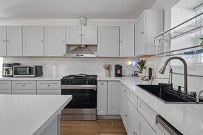 Een moderne keuken met witte kasten, een roestvrijstalen afzuigkap, een magnetron, een fornuis en een spoelbak.