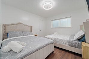 Een slaapkamer met twee bedden, een plafondventilator, een raam met zonwering en een deur.