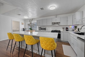 A modern kitchen with white cabinets, a central island with bar stools, stainless steel appliances, and a decorative plant. - Bellaire Spacious 4 Br Home - sleep comfortably for 12 people + (Houston)
