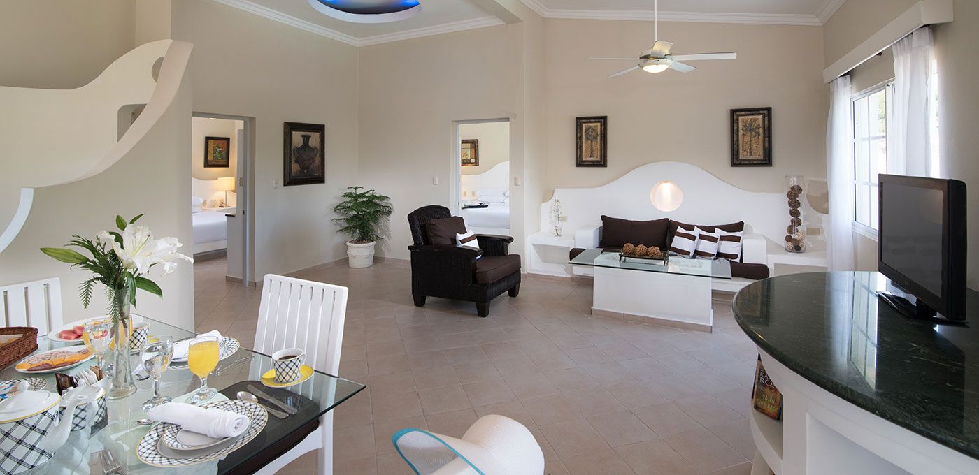 A spacious living area with a dining table set for breakfast, a sofa, a television, and a ceiling fan.