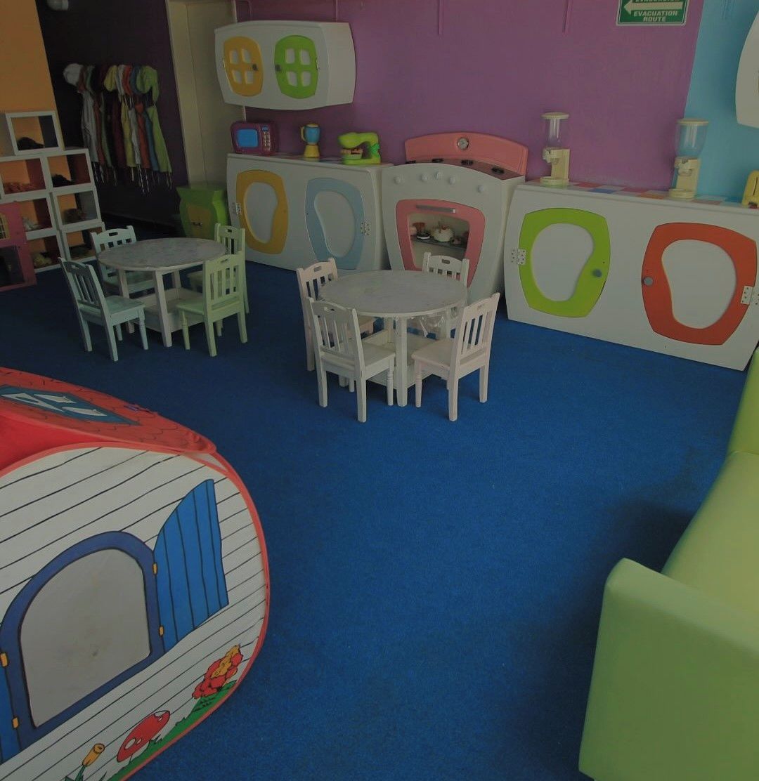 Un área de juegos infantiles con una mesa redonda y sillas, un corralito y unidades de almacenamiento de colores.