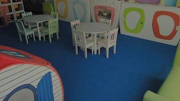 Un área de juegos infantiles con una mesa redonda y sillas, un corralito y unidades de almacenamiento de colores.