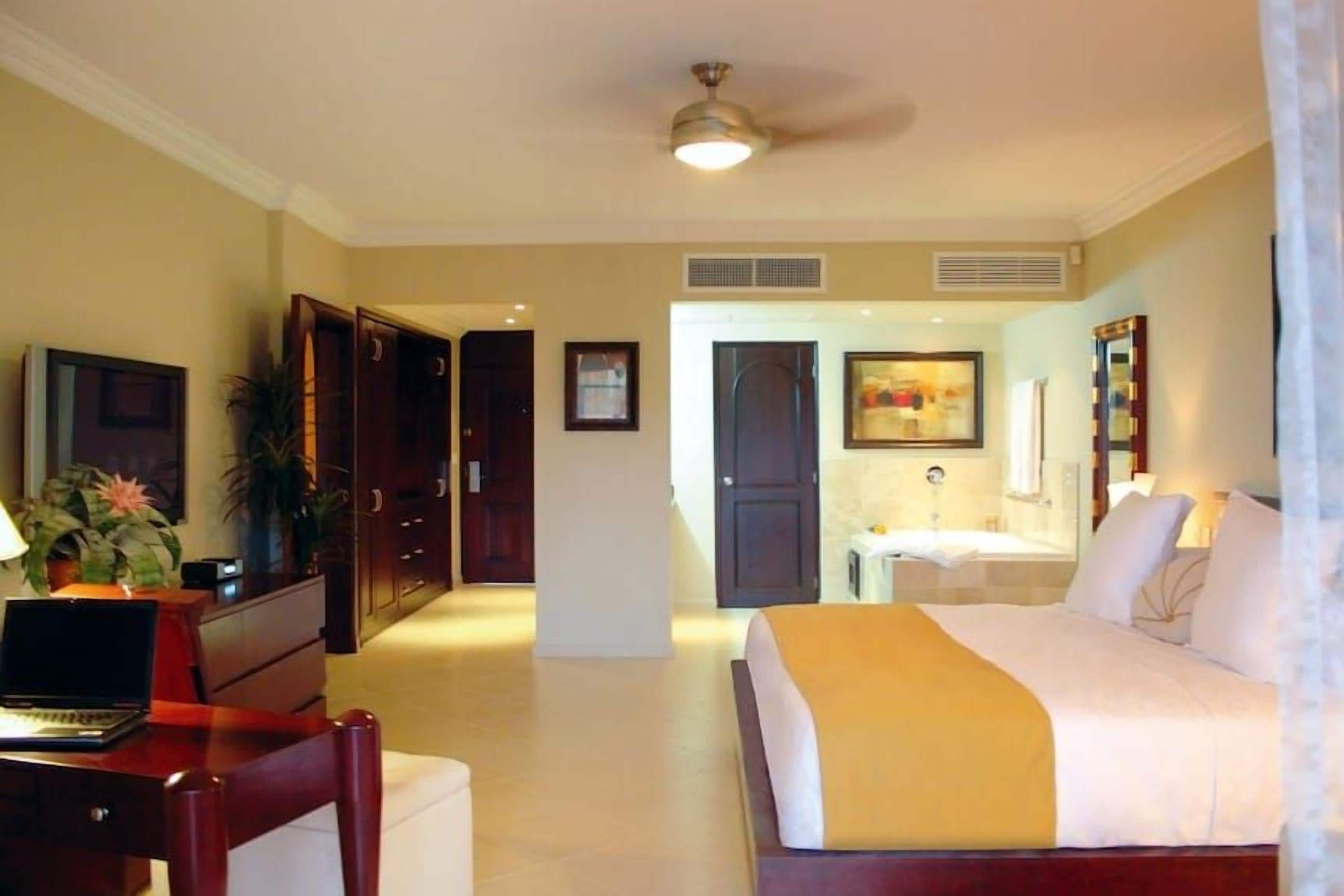 Habitación de hotel con cama, escritorio, silla y baño con lavamanos y espejo.
