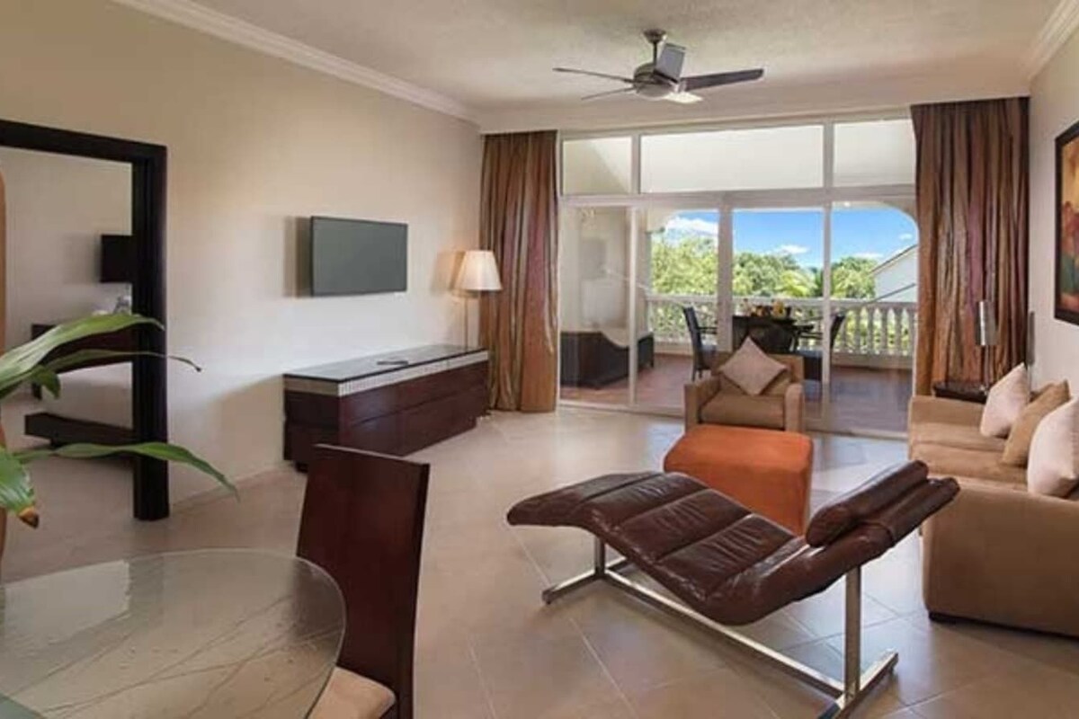 Ein Hotelzimmer mit Balkon, einer Sitzecke, einem Liegesessel, einem Fernseher und einem Schreibtisch.