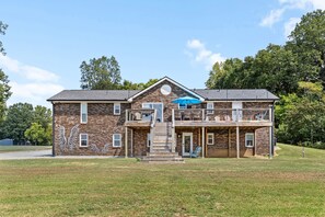 A two-story brick house with a balcony, a front porch, and a mural on the side. - 12-Acre Nashville Retreat - Sleeps 12 - Game Room (Goodlettsville)