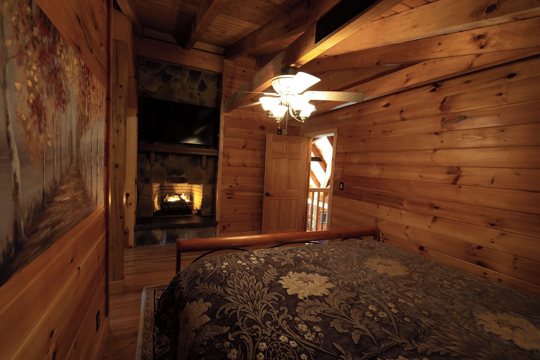 Interior de una cabaña de madera con una cama, chimenea y ventilador de techo.