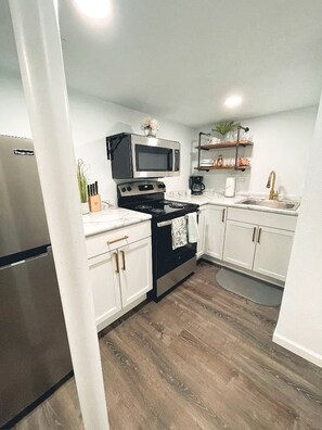 A compact kitchen with white cabinets, a black stove, a microwave, and a stainless steel refrigerator. - Cutest House in the Best Neighborhood in town! (Sioux Falls)