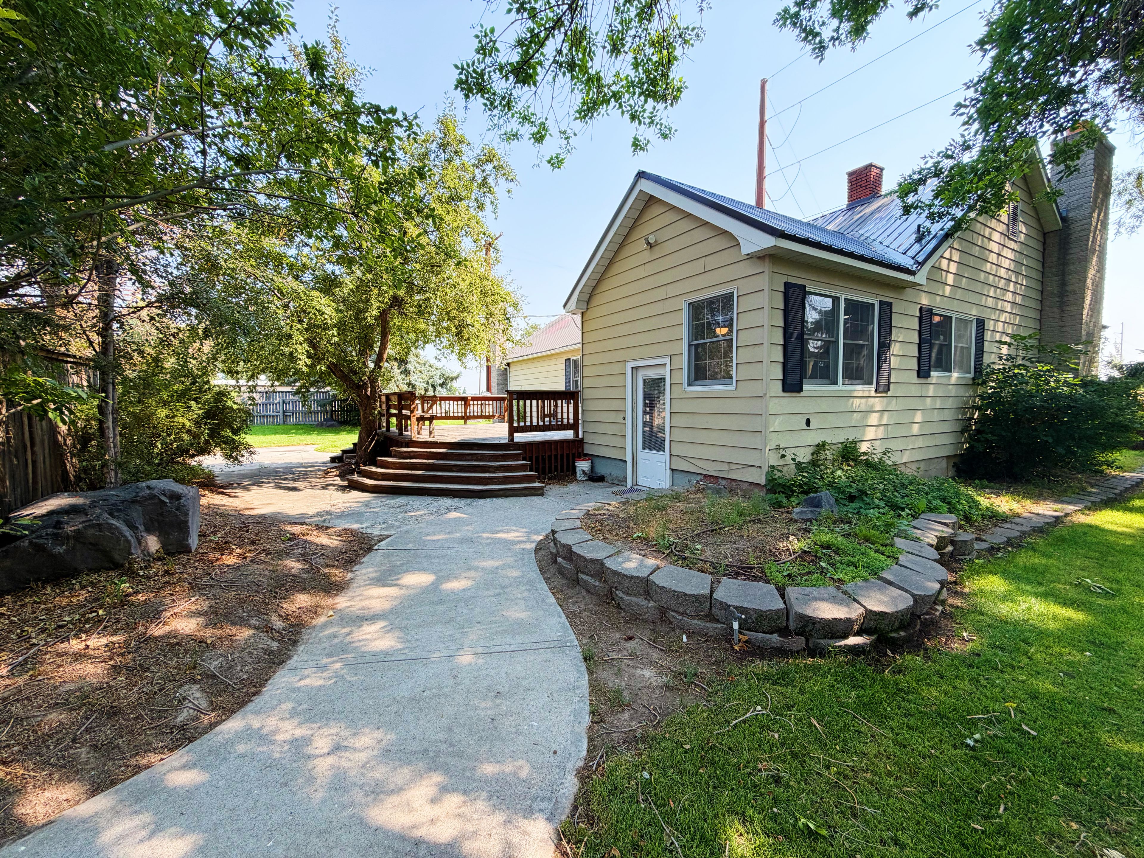 A single-story house with a front porch and a small deck, surrounded by a stone border and a grassy yard.