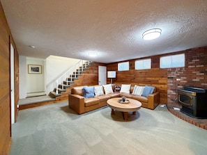 A living room with a brown leather sectional sofa, a round coffee table, a fireplace, and a staircase leading to another level.