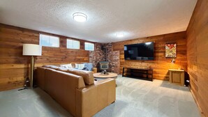 Uma sala de estar acolhedora com um sofá de couro marrom, uma televisão de tela plana, lareira e paredes de madeira.