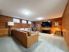 Een gezellige woonkamer met een bruine leren bank, een flatscreen televisie, een open haard en houten wanden.