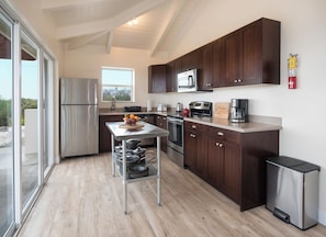 A modern kitchen with stainless steel appliances, wooden cabinets, and a large window. - Harbour Rock Villa – Oceanview Hilltop Villa (PROVIDENCIALES)
