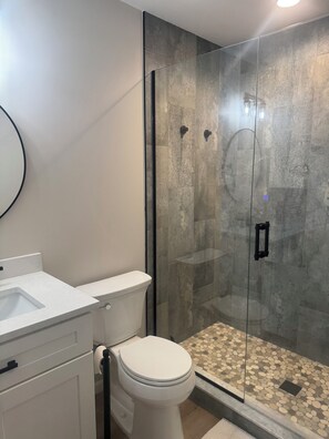 Une salle de bain avec une douche à parois de verre, des toilettes blanches et un lavabo avec un plan de toilette blanc.
