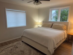 Une chambre à coucher avec un lit, une fenêtre, un ventilateur de plafond et une table de chevet avec une lampe.