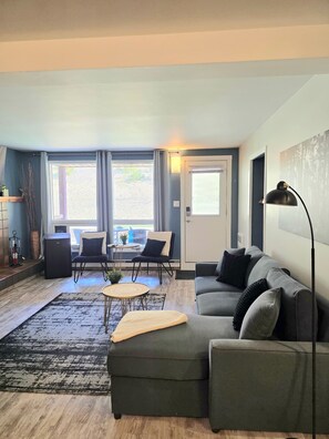 A living room with a grey sofa, a coffee table, and a dining area with chairs and a table. - Panorama Mountain Escape Ski In/Out/Near Hot Tubs (Panorama)