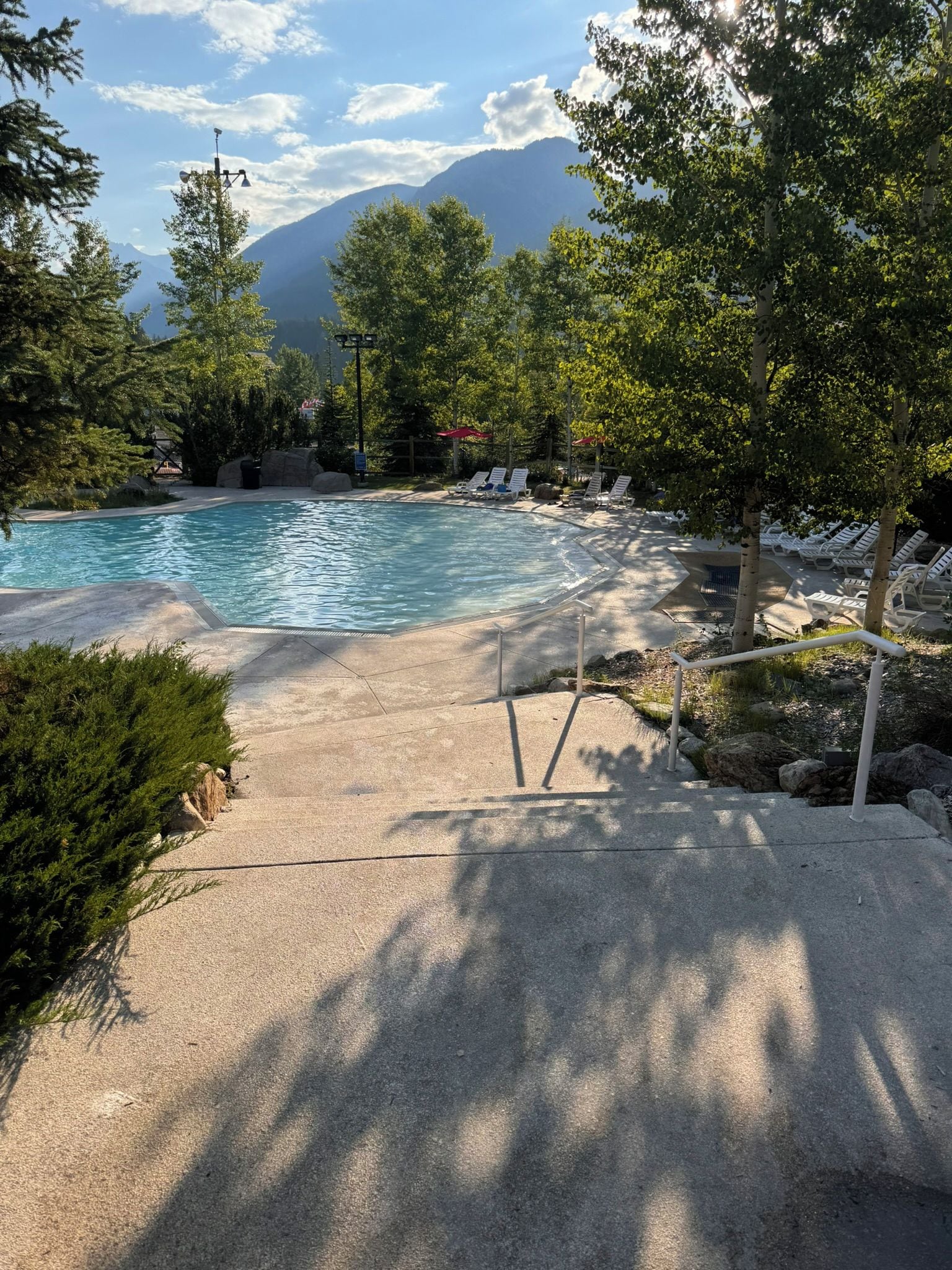 Piscina con sillas de descanso y montañas al fondo.
