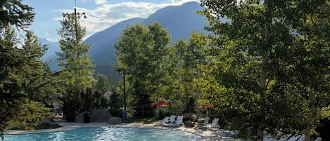 Piscina con sillas de descanso y montañas al fondo.