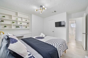 Ein modernes Schlafzimmer mit Bett, Fernseher, einer weißen Ziegelwand und einer Deckenleuchte.