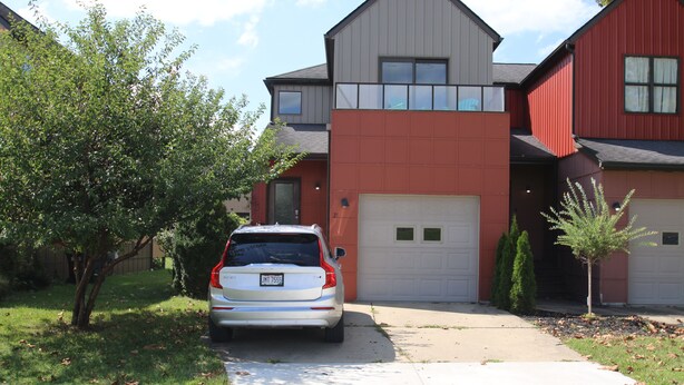 Uma casa moderna de dois andares, com garagem, entrada por automóvel e uma árvore no jardim da frente.