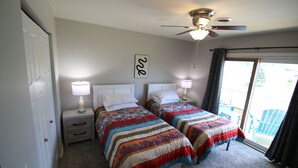 Quarto com duas camas, ventilador de teto e janela com cortinas.