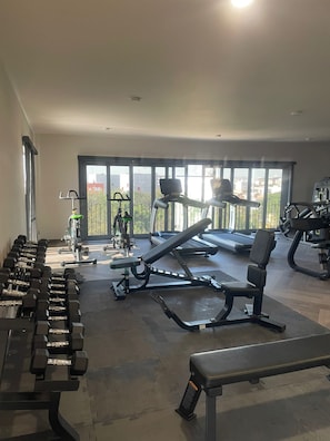 Un gimnasio con equipamiento de ejercicio, una banca y una cinta de correr.