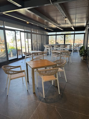Een ruime binnenruimte met meerdere tafels en stoelen, grote ramen met uitzicht op de stad, en een modern plafondontwerp.
