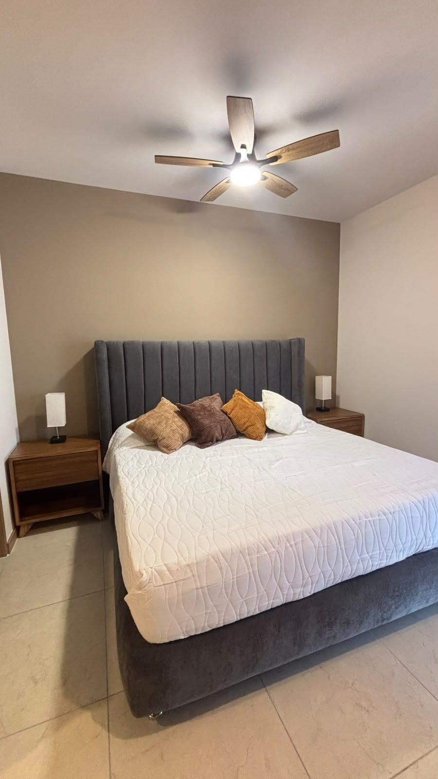 A bedroom with a bed, a ceiling fan, and a nightstand with a lamp.