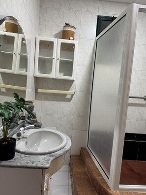Ein Badezimmer mit Waschbecken, Spiegel, Schränken und einer Duschkabine.