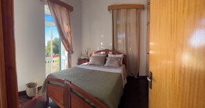 Ein Schlafzimmer mit einem hölzernen Bett, einem Nachttisch, einem Fenster mit Vorhängen und einer Tür.