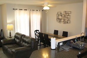 A living room with a leather sofa, a dining table with chairs, a kitchen area with a bar, and a ceiling fan. - Great townhouse in Athens, 3 bedrooms, 5 beds, garage, Wi-Fi, bike path (Athens)