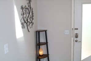 Ett rum med en vit dörr, en väggdekoration i form av ett träd och en trähylla med en lampa.