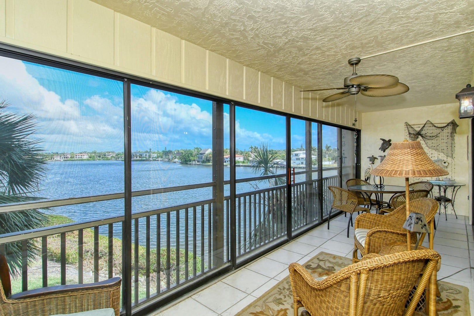 A room with large windows overlooking a body of water, wicker furniture, and a ceiling fan.