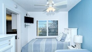 Un dormitorio con cama, mesita de noche, lámpara, televisor y ventana con persianas.