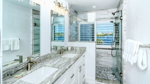 Un baño moderno con dos lavabos, cabina de ducha con mampara de vidrio y vistas al mar.