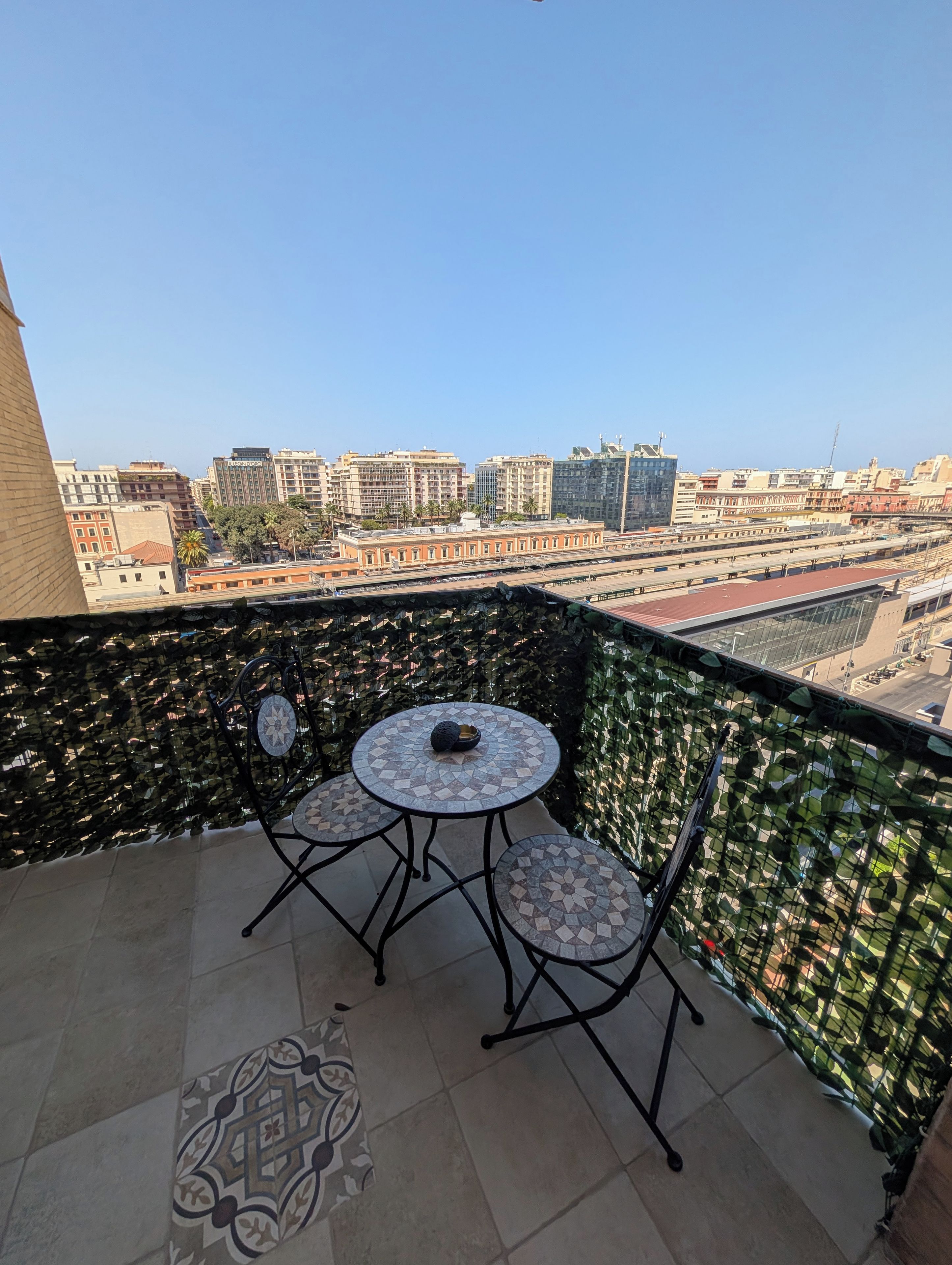 Un balcone con tavolo e sedie, un pavimento decorato e vista sulla città, con edifici e un ponte.