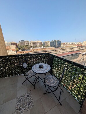 A balcony with a table and chairs, a patterned floor, and a view of a cityscape with buildings and a bridge. - Private Suite Facing Bari Centrale Station: Elegant and Meticulously Designed Down to the Last Detail (Bari)